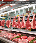 Meat hanging on hooks in a supermarket or refrigerated warehouse with steel rail system overhead for storage.