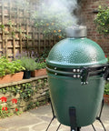 Medium Big Green Egg grill with hinge assembly replacement kit, showing powder coated steel hinge and spring in a garden setting.