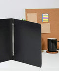Open black folder with Premium 3 Inch Capacity Metal Prong Paper Fasteners Pack Of 50 With 8.5 Inch Base on a desk near a corkboard.
