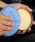 Person holding Microfiber Wax Applicator Pads For Car Detailing 5 Inch Foam Buffing Pads With Built In Sponge High Absorbency And Elastic Sponge Layer Ideal For Applying Waxes Polishes Protectants And Dressings 6 Pack next to car wax tin