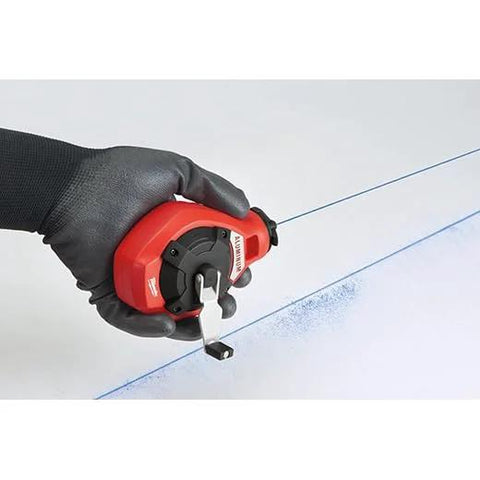 Hand using Milwaukee Chalk Line Reel Set F with 100 ft blue line for marking on surface, showing precise layout application.