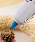 Applying AdTech High Temp Mini Glue Sticks Five Sixteenths Inch By Four Inch 100 Pack For Hot Glue Guns to a pinecone with burlap in background.
