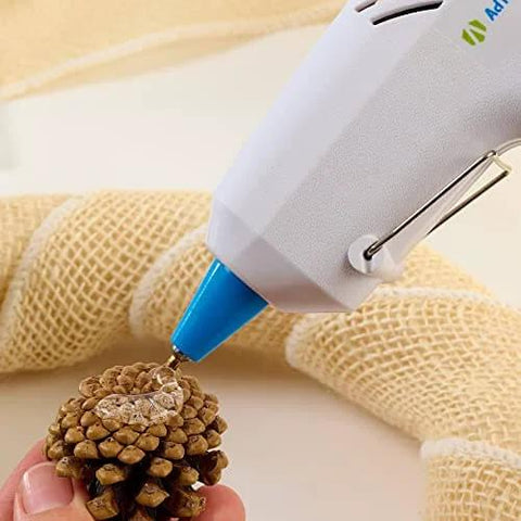 Applying AdTech High Temp Mini Glue Sticks Five Sixteenths Inch By Four Inch 100 Pack For Hot Glue Guns to a pinecone with burlap in background.