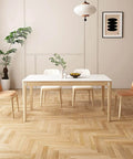 Minimalist dining room with white table, four chairs, wood floor, plants, and abstract wall art.