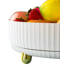 Decorative white ceramic fruit bowl with gold accents filled with assorted fruits.