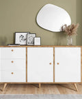 Modern sideboard with white doors and natural wood details, featuring decor items and a mirror on the wall behind.