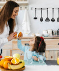 Mother and daughter in modern kitchen with fruit on table, smiling and preparing food, utensils hanging on wall, warm family moment.