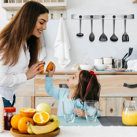 Mother and daughter in modern kitchen with fruit on table, smiling and preparing food, utensils hanging on wall, warm family moment.