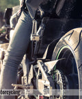 Close-up of motorcycle rear wheel and rider's leg, focus on tire and chain, outdoors.