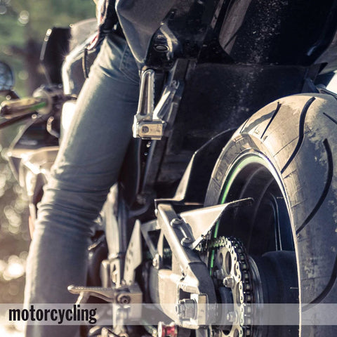 Close-up of motorcycle rear wheel and rider's leg, focus on tire and chain, outdoors.