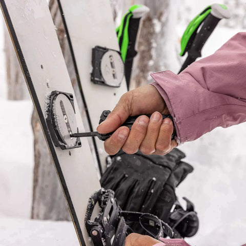 Person using Suspension-NXT 15-In-1 EDC Multi Tool to adjust snowboard bindings in snowy outdoor setting