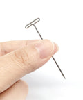 Hand holding a single 2 Inch T Pins Set Of 100 Nickel Plated Steel Pins with 14 mm head for knitting, wigs, sewing, and crafting projects.