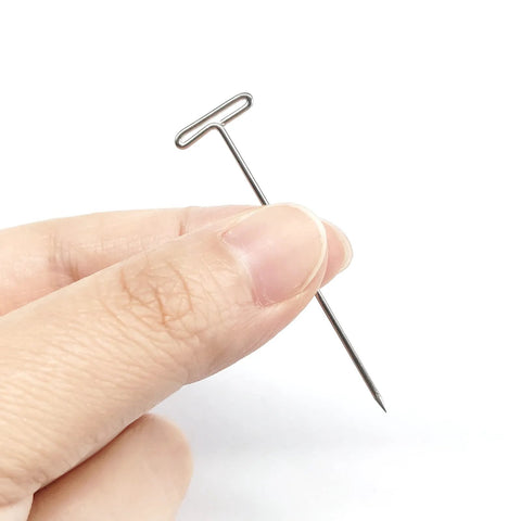 Hand holding a single 2 Inch T Pins Set Of 100 Nickel Plated Steel Pins with 14 mm head for knitting, wigs, sewing, and crafting projects.