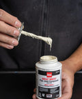 Hands showing Oatey Non Toxic Non Hardening White Pipe Joint Compound for Threaded Joints, 4 oz jar with lid applicator.