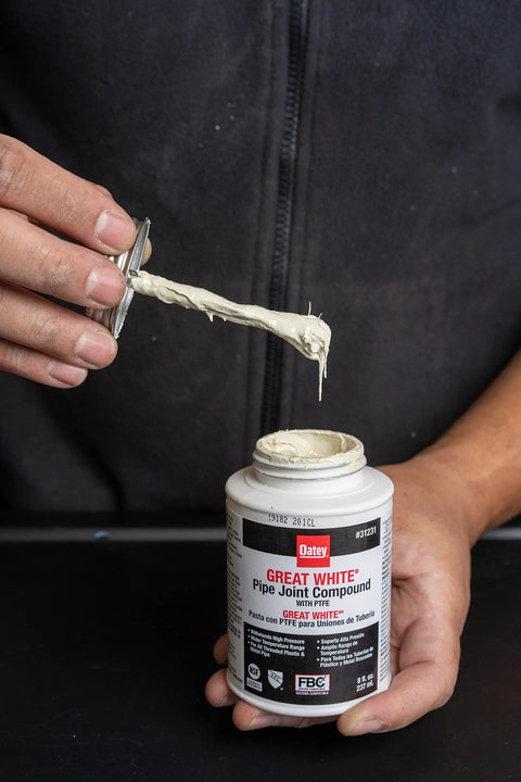 Hands showing Oatey Non Toxic Non Hardening White Pipe Joint Compound for Threaded Joints, 4 oz jar with lid applicator.
