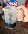 Hand holding Two Stroke Oil Measuring Cup 16 Oz Mixing Pitcher with 15 In 1 Ratio Conversion Chart in a workshop
