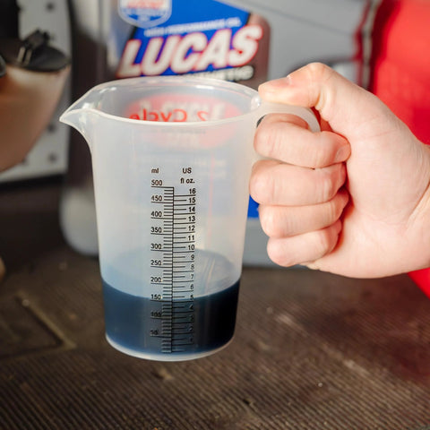 Hand holding Two Stroke Oil Measuring Cup 16 Oz Mixing Pitcher with 15 In 1 Ratio Conversion Chart in a workshop