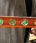 Person holding Savage 9 Inch Magnetic Torpedo Level With Four Neodymium Magnets And Four Vials For 30 Degree Conduit Bends Built From Solid Aluminum For Lifetime Durability Bright Orange Finish For Easy Visibility On Any Job Site.