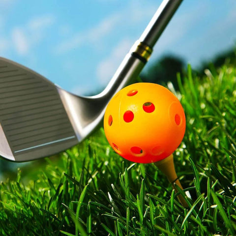 Orange Practice Golf Training Ball on tee, close-up view, with a golf club on grass. Limited Flight 40mm Hollow Plastic Colored Airflow Golf Balls.