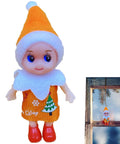 Festive elf doll in orange and white outfit with Christmas tree design and red shoes, next to window display with holiday decor.