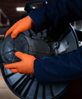 Worker using Hi Vis Orange Nitrile Gloves Raised Diamond Texture 8 Mil Large Box Of 50 while handling machinery in a workshop.