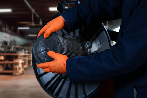 Worker using Hi Vis Orange Nitrile Gloves Raised Diamond Texture 8 Mil Large Box Of 50 while handling machinery in a workshop.