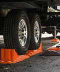 Interlocking RV Leveling Blocks 10 Pack With Nylon Storage Bag For Trailer Motorhome And Vanlife Up To 40,000 Lbs Capacity Orange in use under RV tires, stabilizing on uneven terrain.