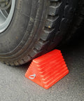 Heavy Duty Orange Wheel Chocks 2 Pack With Eyebolt For Travel Trailer 10 Inch Long 8 Inch Wide 5.7 Inch High Durable Structural Foam Chocks For Safe Parking holding a vehicle tire.