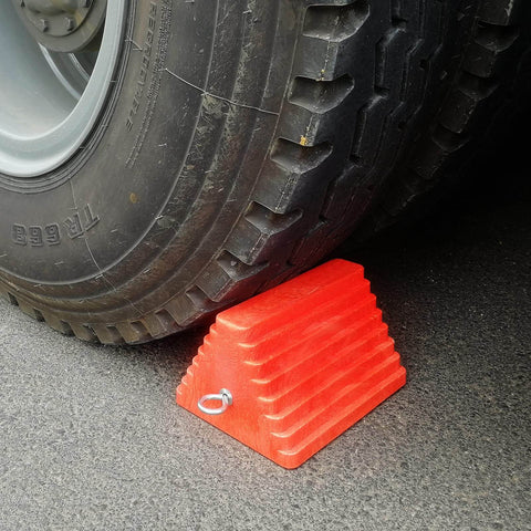 Heavy Duty Orange Wheel Chocks 2 Pack With Eyebolt For Travel Trailer 10 Inch Long 8 Inch Wide 5.7 Inch High Durable Structural Foam Chocks For Safe Parking holding a vehicle tire.