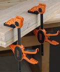 Two Pack Six Inch One Hand Clamp and Spreader Set with 300 lb clamping force attached to a wooden table, orange and black