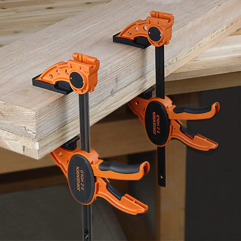 Two Pack Six Inch One Hand Clamp and Spreader Set with 300 lb clamping force attached to a wooden table, orange and black