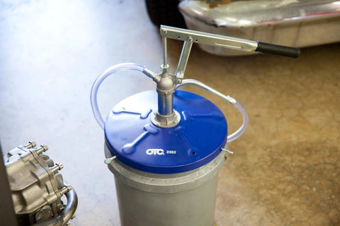 OTC 2352 Lever Action Bucket Pump on a 5-gallon pail, featuring a lever handle, blue drum cover, and discharge hose