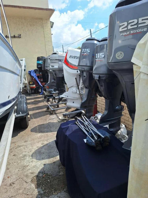 Row of outboard boat motors in an outdoor storage area next to a building wall, beside parked boats.