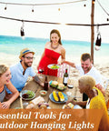 Group of friends dining at a beach table with drinks and food, under hanging outdoor lights, enjoying a cheerful gathering.