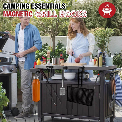 Two people using a grill station with various camping essentials, featuring magnetic grill hooks holding tools.