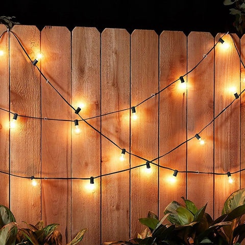 Outdoor string lights hanging on a wooden fence at night