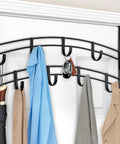 Over-the-door black metal coat rack with multiple hooks holding coats, a blue shirt, an umbrella, and a keychain on a white door.