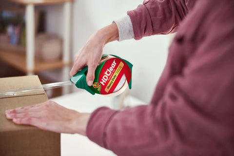 Person using HD Clear Packing Tape Dispenser Heavy Duty Tape Gun for Boxes Shipping and Moving Includes One Refill Roll Foam Handle.