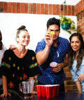 Group playing party game with 100 Pack Table Tennis Balls, 40mm Colored Plastic Balls Beer Balls Bulk; yellow ball in focus.