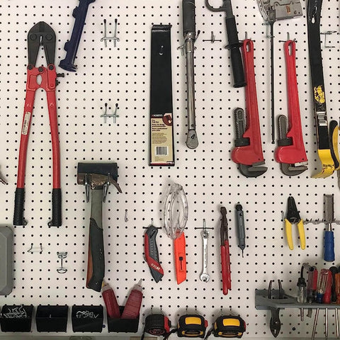 Assorted hand tools including wrenches, pliers, and hammers organized on a pegboard in a garage or workshop setting.