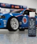 Permatex 81950 Ultra Slick Engine Assembly Lube, 4 oz. , Red bottle in front of a blue racing car in a garage setting.