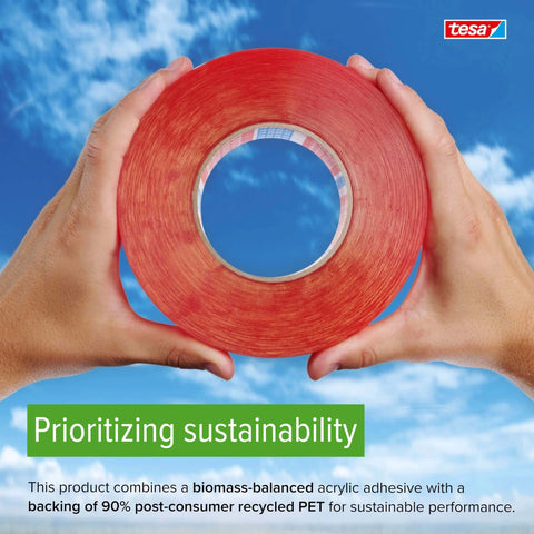 Hands holding a roll of red double-sided tape with a blue sky background, emphasizing sustainable materials and branding.