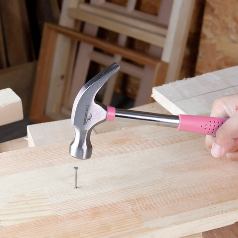 8 oz claw hammer with a shock-absorbing non-slip pink grip used for driving a nail into wood with durable steel head and claw