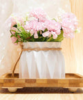 Pink flowers in white vase on wooden tray with fabric background
