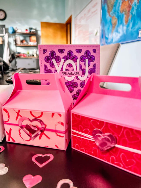 Pink and red decorative gift boxes with heart patterns and a purple 'You Are Awesome' card in a home office setting.