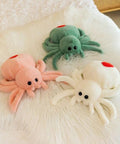 Trio of colorful plush spider toys with red spots on a soft surface, showcasing playful design and cuddly texture.