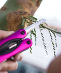 Using Pink 14-In-1 Aluminum Multi-Tool with stainless steel saw blade for pruning branches during camping or everyday tasks.