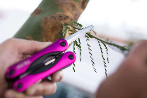 Using Pink 14-In-1 Aluminum Multi-Tool with stainless steel saw blade for pruning branches during camping or everyday tasks.