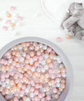 Overhead view of Plastic Balls for Ball Pits - Pack of 100 Hollow Balls, in pink, gold, pearl white, and clear, next to a plush elephant toy.