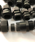 Assorted black plastic cable glands with threaded connectors and labels, arranged on a white surface.